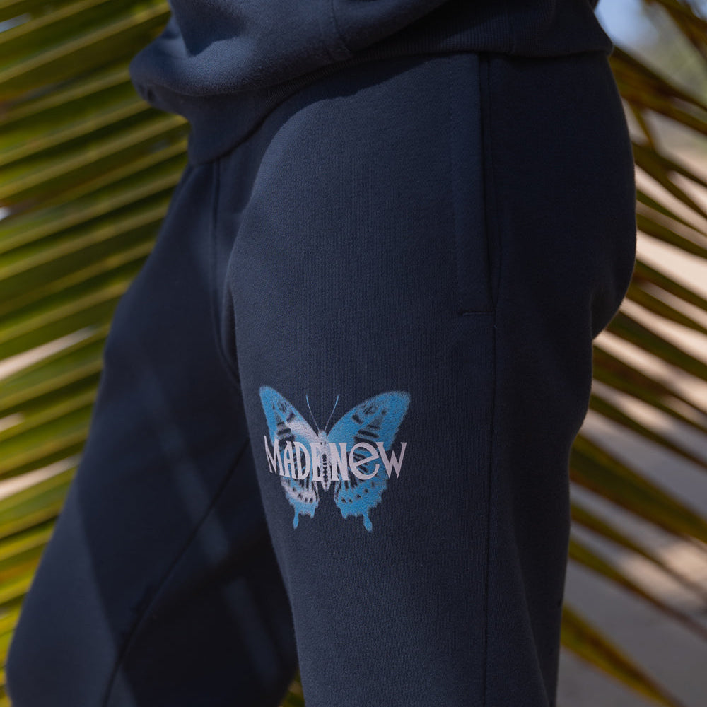 Black hoodie with a blue butterfly logo on the sleeve against a palm leaf background
