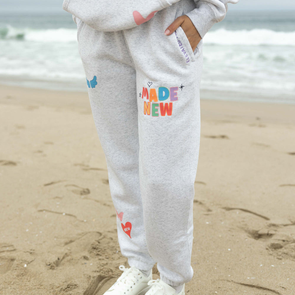 Person wearing gray sweatpants with colorful text on a beach