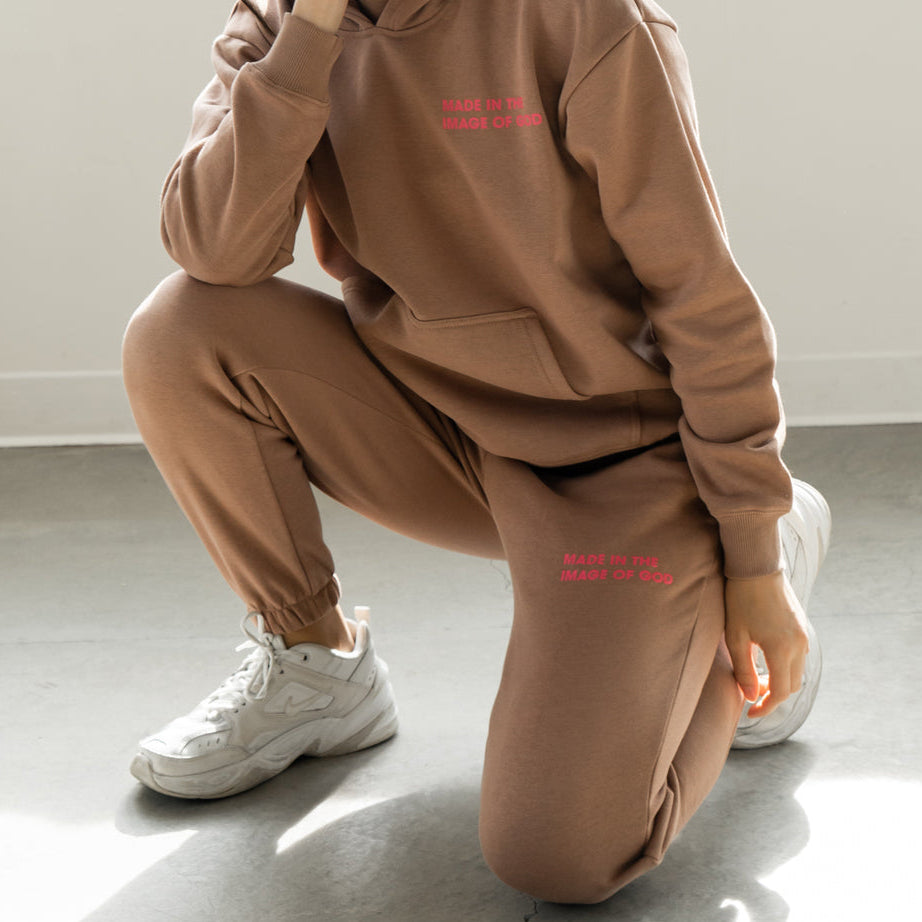 Person wearing a brown hoodie and pants with red text, sitting on the floor.