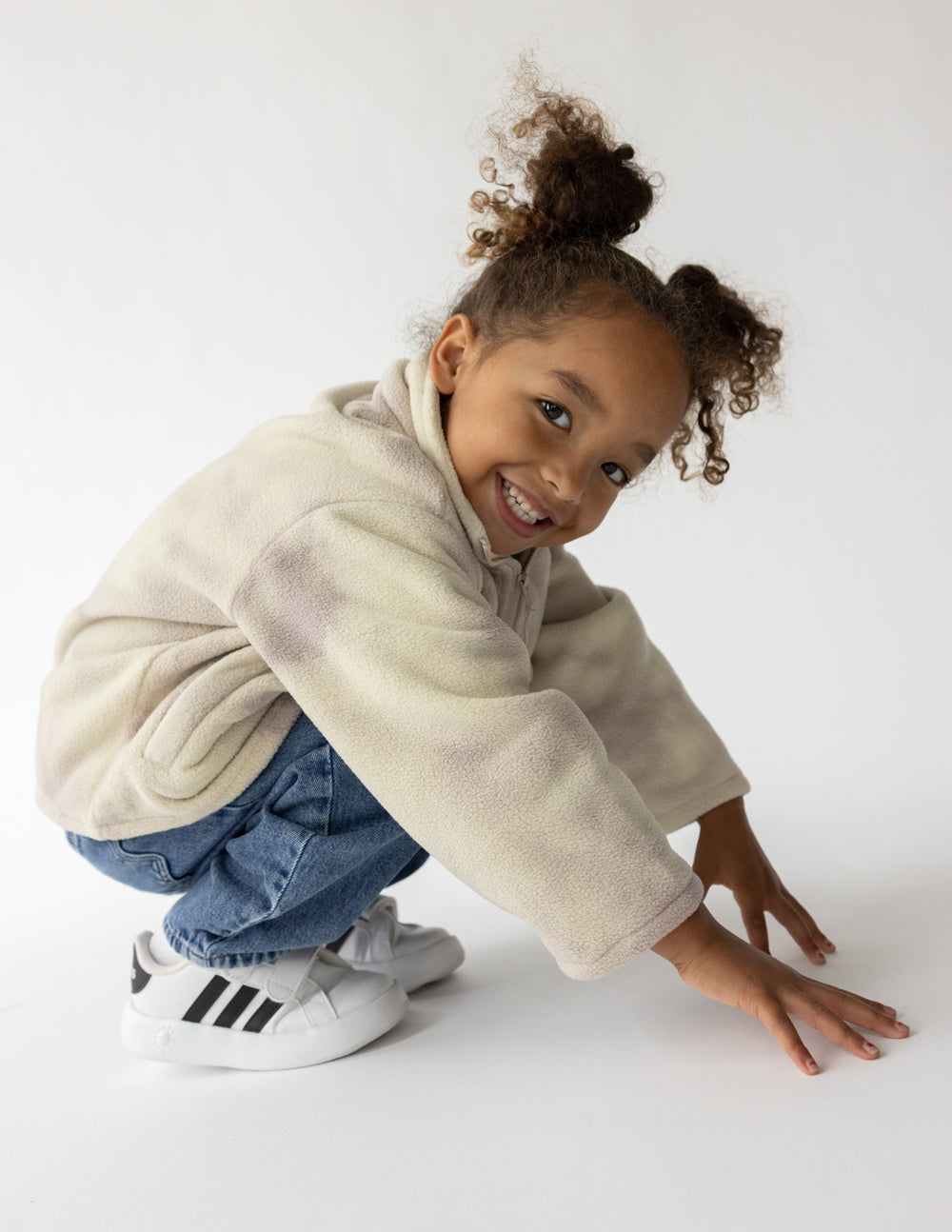 Child crouching in a pearl and mauve marble fleece pullover with jeans and sneakers