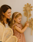 Woman and young girl interacting with decorative rattan flowers in a home setting