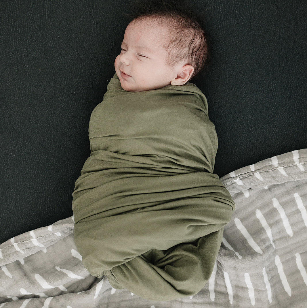 Newborn baby wrapped in a green swaddle on a dark background