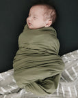 Newborn baby wrapped in a green swaddle on a dark background
