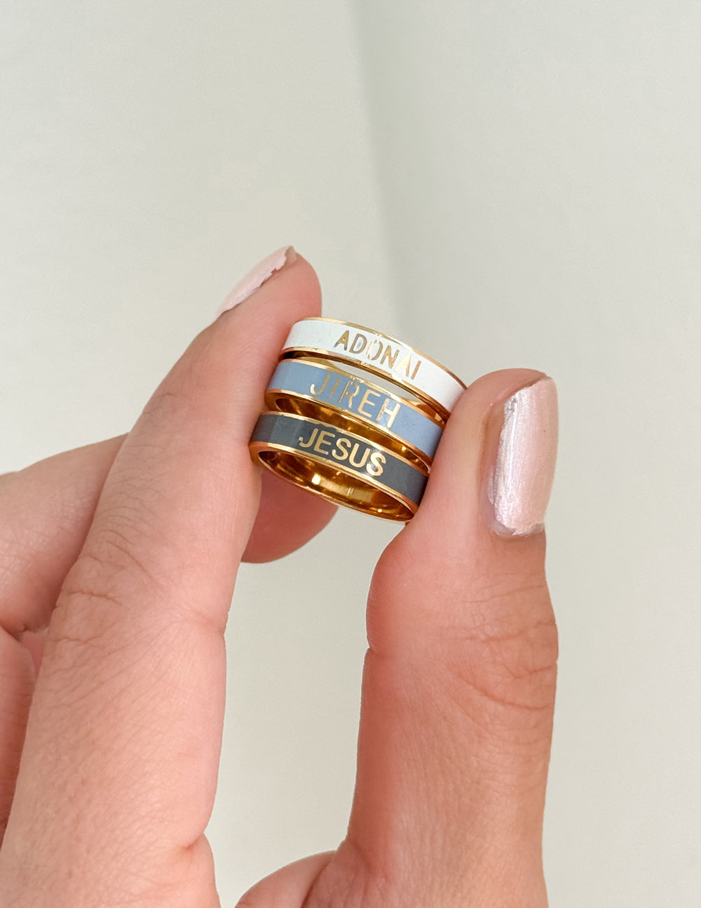 Names of God Enamel Ring Set held between fingers, showing three coordinating bands with gold-tone details