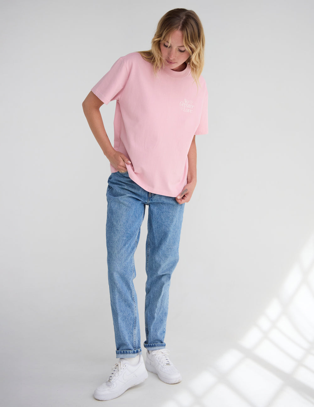 Full-length front view of a woman wearing the oversized Nectar pink T-shirt with jeans and white sneakers