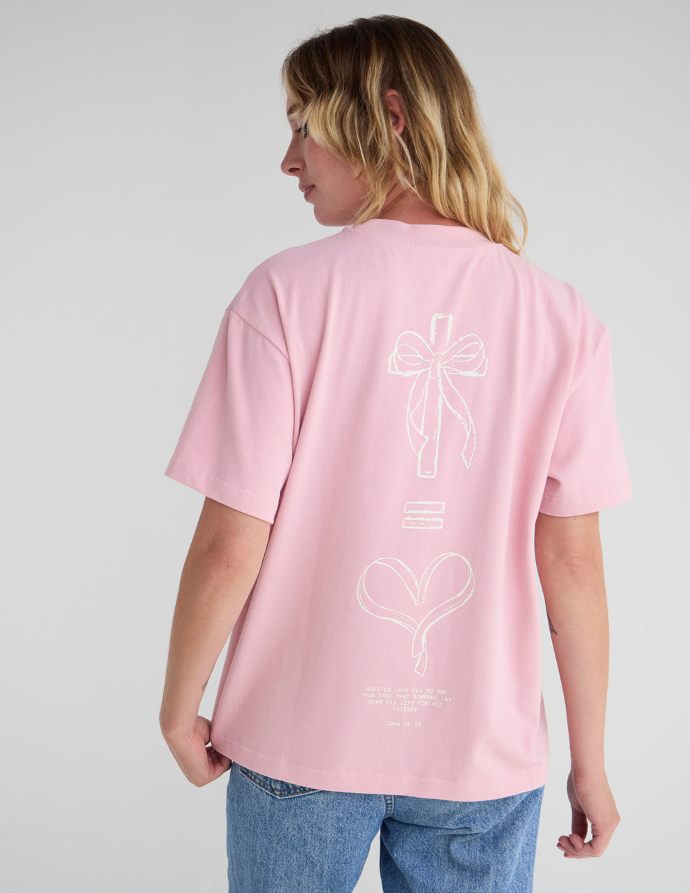 Angled back view of the No Greater Love pink T-shirt showing its cross and heart artwork