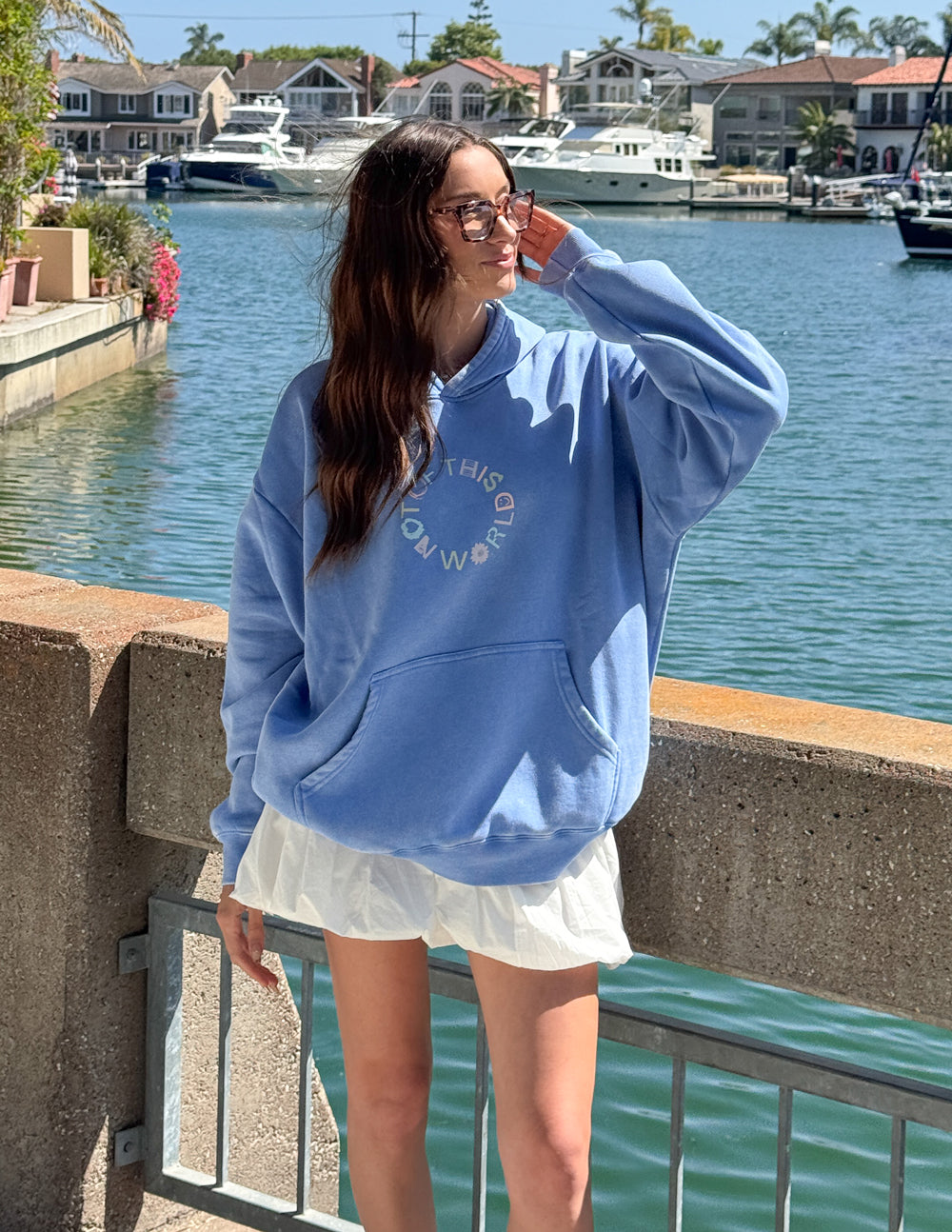 Model wearing the Not of This World blue hoodie with light-colored shorts beside the water
