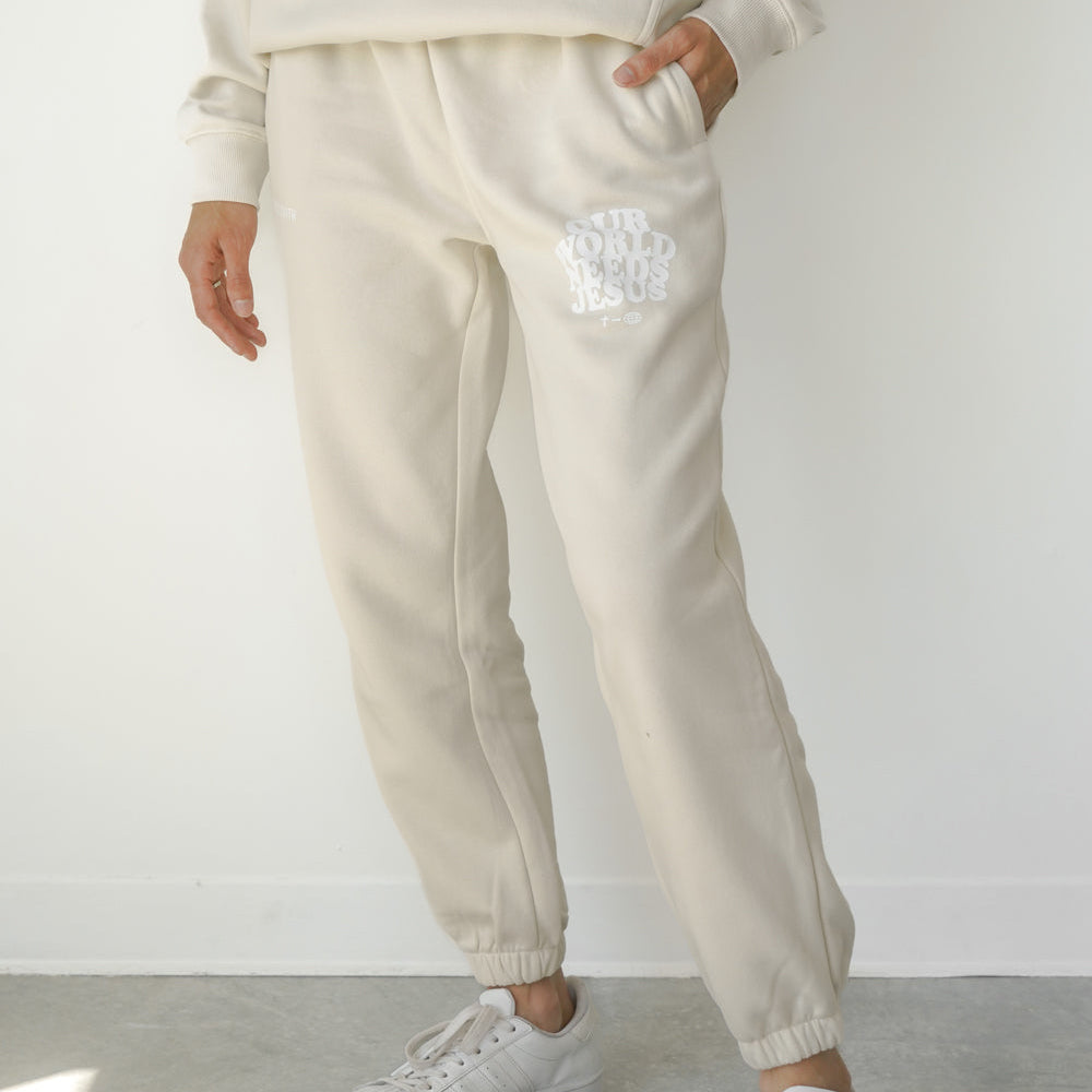 Person wearing a cream-colored tracksuit with white sneakers on a plain background