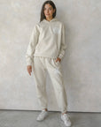 Person wearing a beige tracksuit with a logo against a plain background