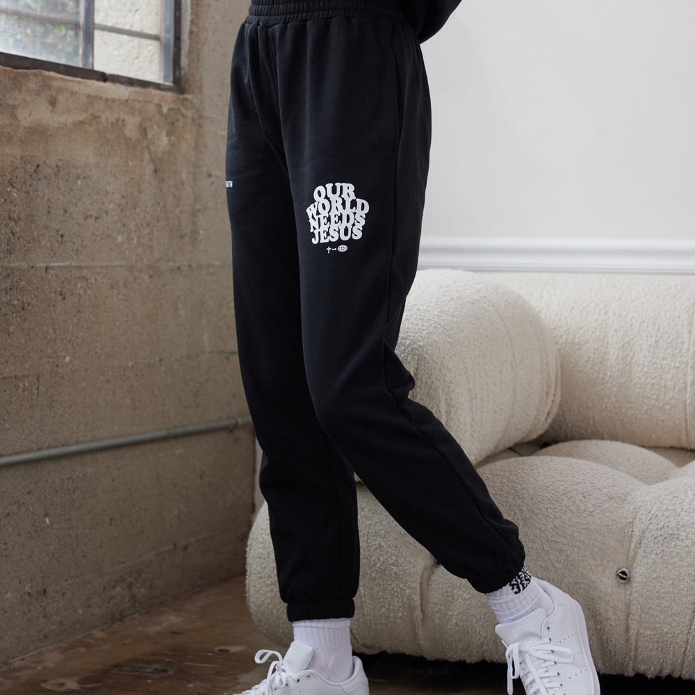 Person wearing black sweatpants with text and white sneakers in a room.