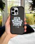 Hand holding the Our World Needs Jesus iPhone case near a window with greenery outside
