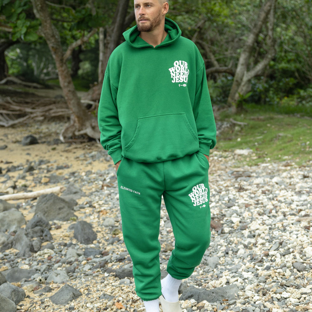 Man wearing a green tracksuit with a logo, standing on a rocky beach.