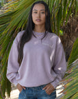 Front view of a woman wearing the Peace of God Vintage Orchid Crewneck Sweatshirt with blue jeans outdoors