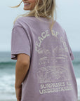 Woman wearing a purple t-shirt with a beach graphic and text on a beach background