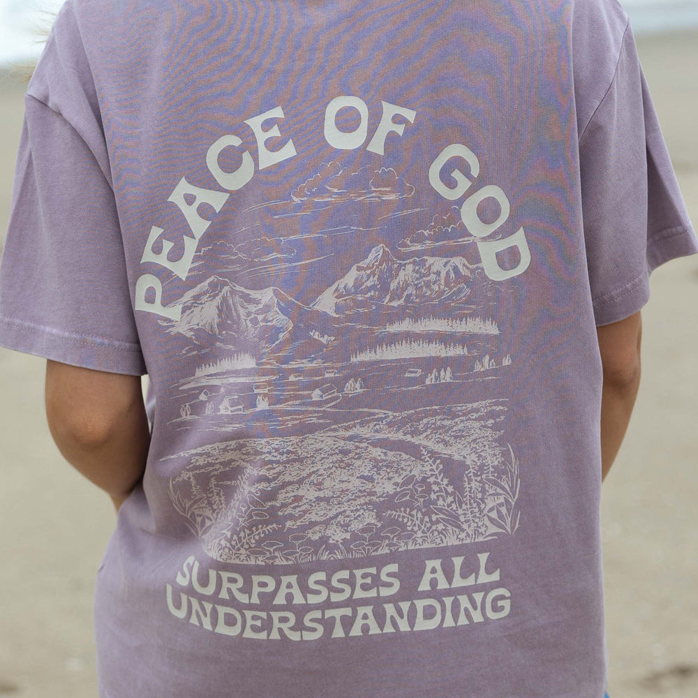 Person wearing a purple t-shirt with a scenic design and text on a beach.