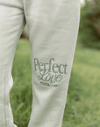 Light-colored pants with 'Perfect Love' text on a grassy background