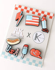 Set of colorful pins on a checkered card with visible brand logos.