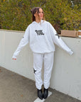 Woman wearing Pray First Heather Grey Hoodie with black lettering and sleeve star graphics outdoors