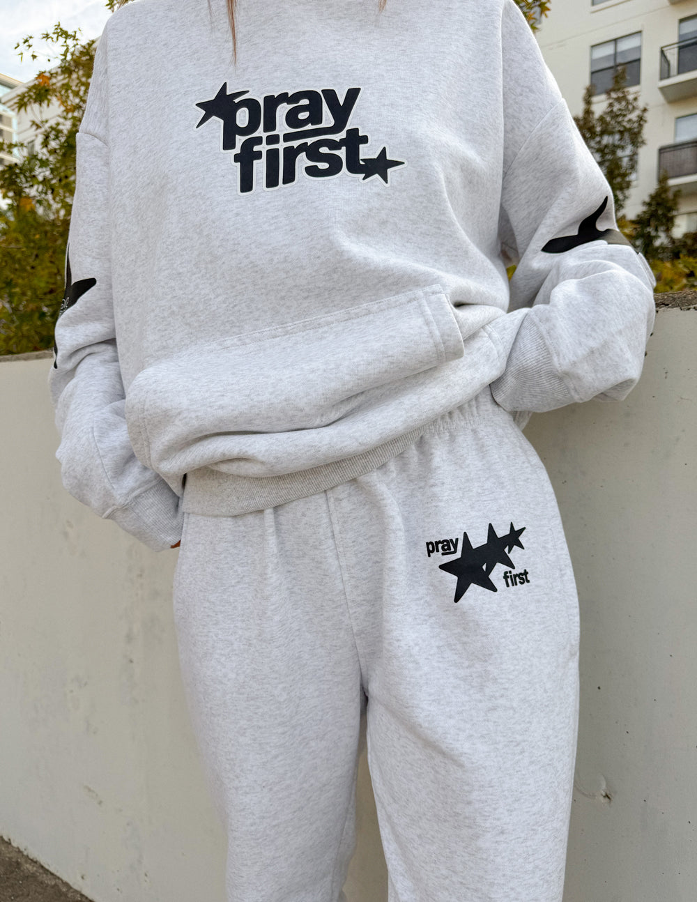Close-up of Heather Grey Pray First sweatpants with black star graphics, styled with a coordinating hoodie.