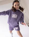 Child wearing the Eggplant purple Prayer Works hoodie with cream lettering and coordinating shorts.