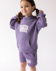 Child holding the hood of the Eggplant Prayer Works hoodie.