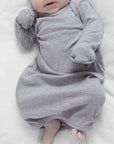 Baby in a gray onesie lying on a white blanket