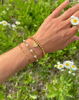 Renewal gold-tone bracelets stacked on a wrist above grass and small white flowers