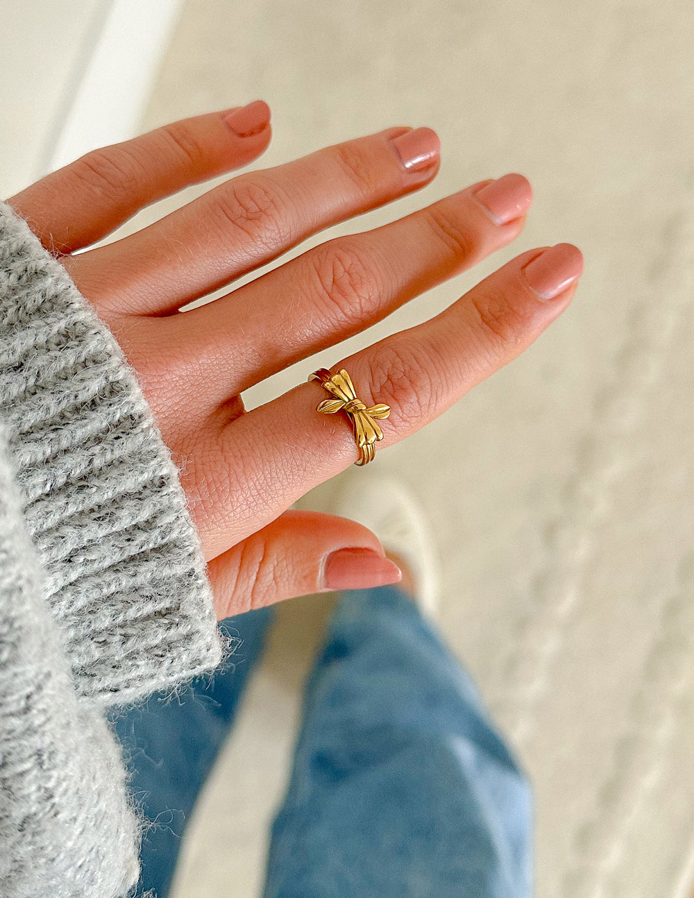 Hand wearing the gold-tone Ribbon Bow Ring beside a gray sweater sleeve.
