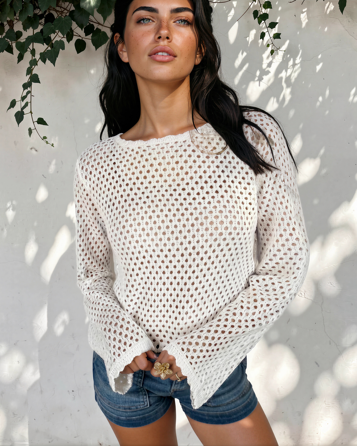Model wearing the white Felicity open-knit top with a round neckline and long sleeves, styled with denim shorts.