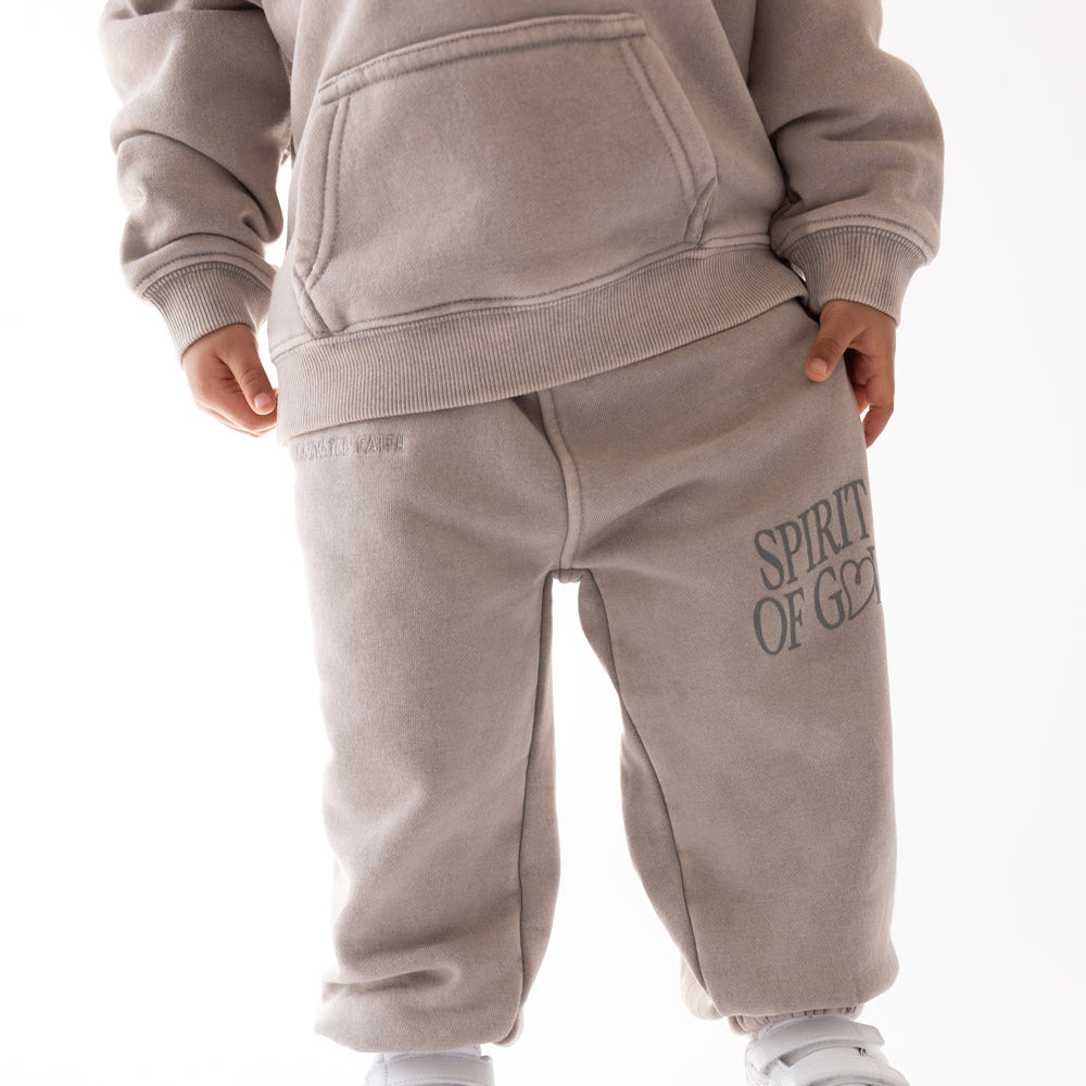 Child wearing a beige tracksuit with 'Spirit of Good' text on pants against a white background