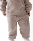 Child wearing a beige tracksuit with 'Spirit of Good' text on pants against a white background