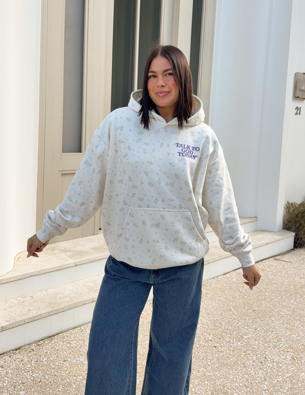 Model wearing the ivory Talk to God Allover Wildflower Unisex Hoodie with blue jeans