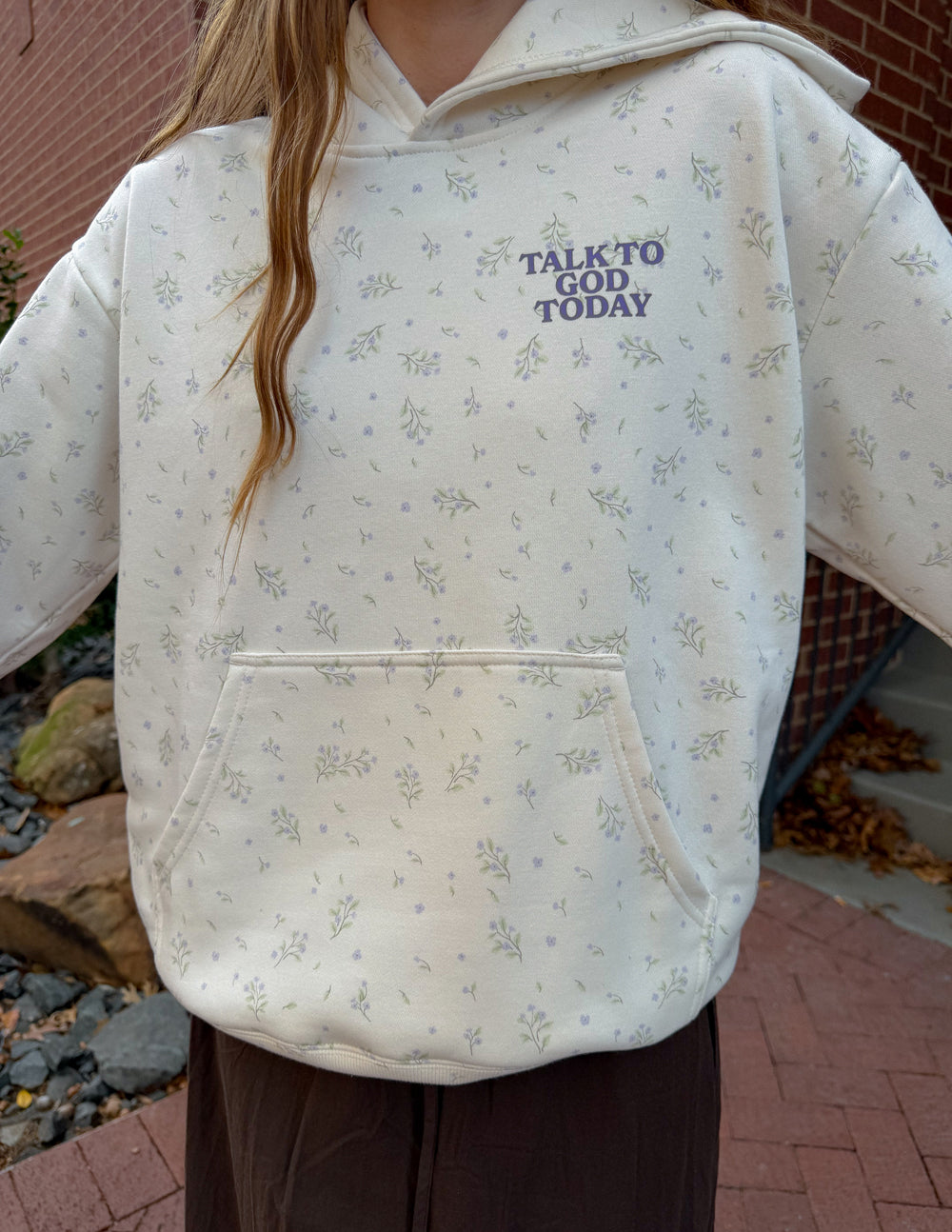 Close-up of the ivory Talk to God hoodie showing the wildflower print, chest lettering, and kangaroo pocket