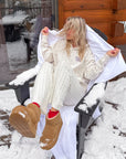 Model seated outdoors in the snow wearing the ivory Talk to God wildflower hoodie
