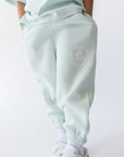 Light blue sweatpants with a logo worn by a person on a white background