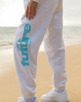 Person wearing gray sweatpants with 'Futile' branding on a beach.