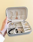 Open jewelry travel case held against a yellow background with necklaces, bracelets, and rings arranged inside