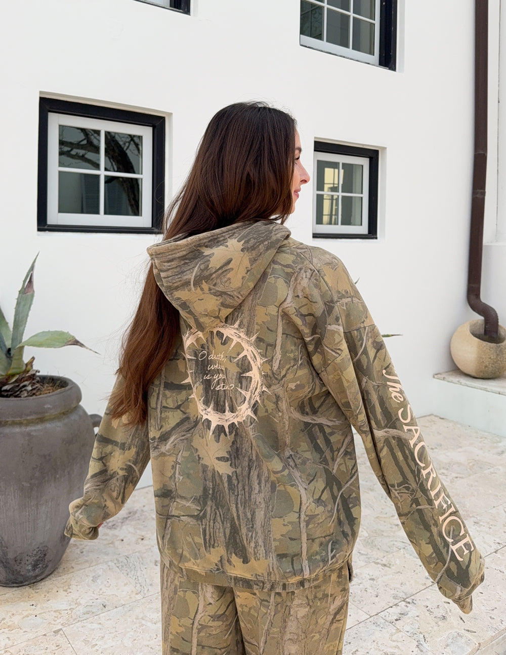 Model wearing The Sacrifice Forest Camo hoodie with a large crown-of-thorns design on the back