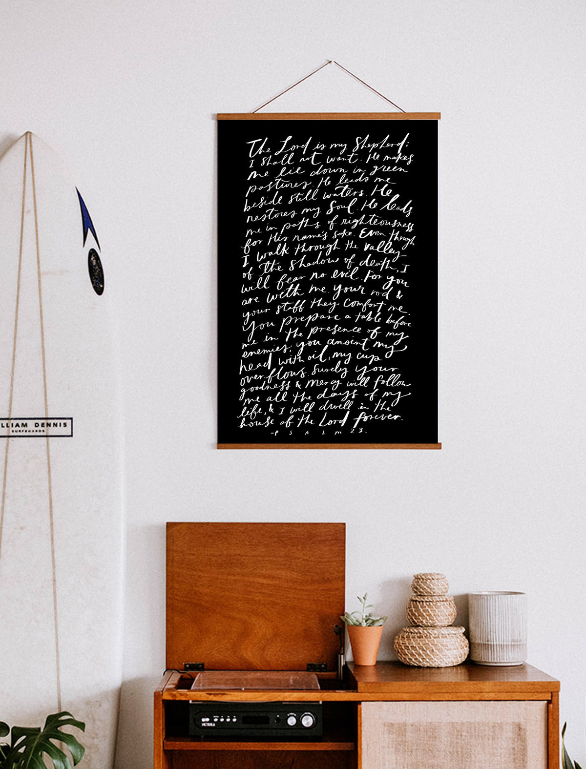 Black Psalm 23 scripture poster with white lettering and wooden hanging rails above a wooden cabinet.