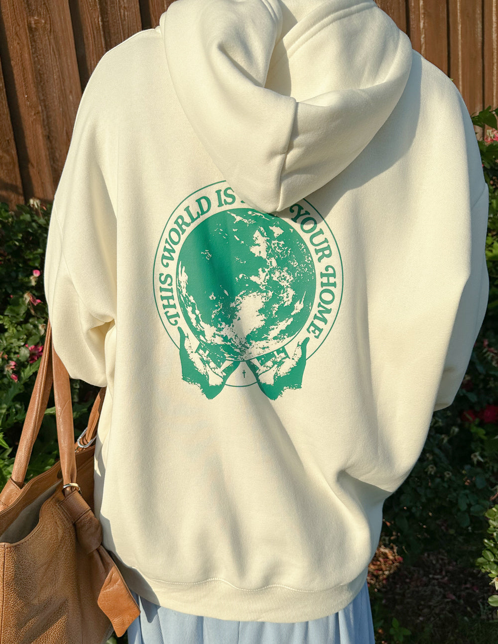 Close-up of the hoodie’s large green globe back graphic outdoors beside a wooden fence.