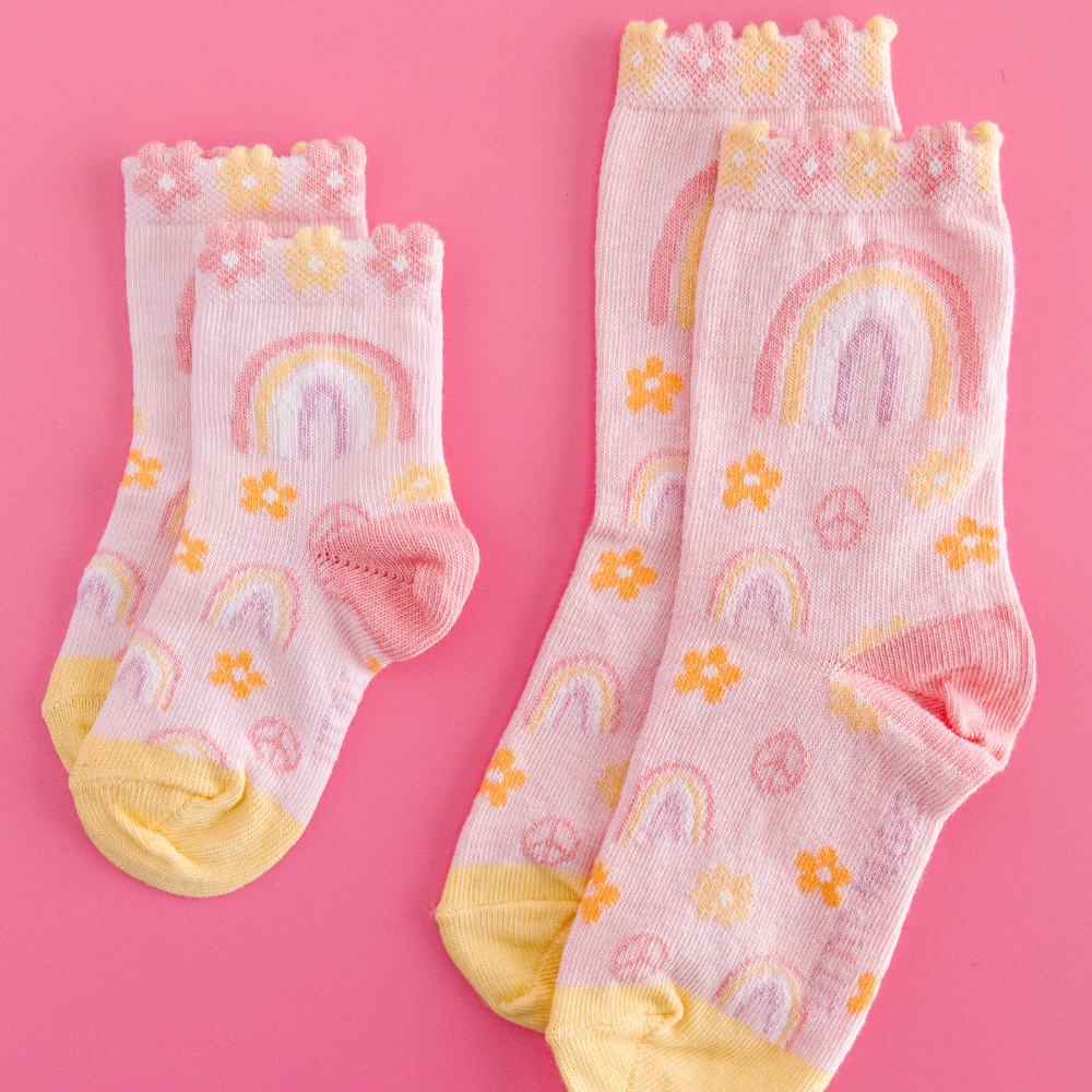Two pairs of children's socks with rainbows and flowers on a pink background