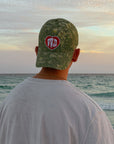 Rear view of a model wearing the WWJD camouflage baseball cap beside the ocean