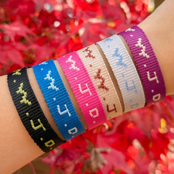 Wrist wearing multiple colorful woven bracelets with a blurred red floral background