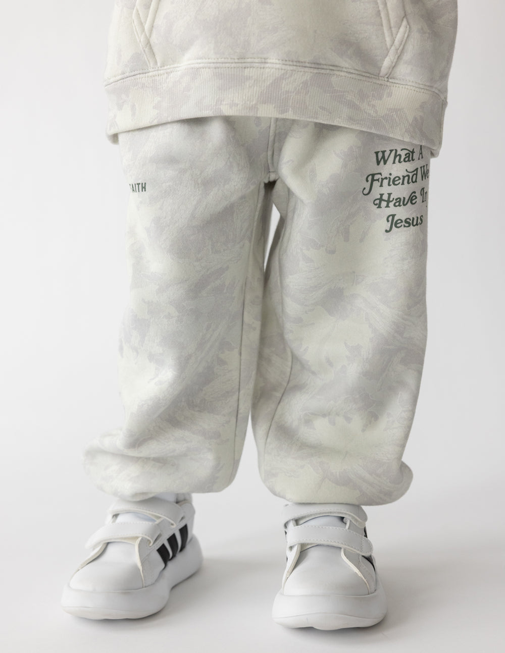 Front view of white camo kids’ sweatpants with What a Friend We Have in Jesus lettering, worn with white sneakers