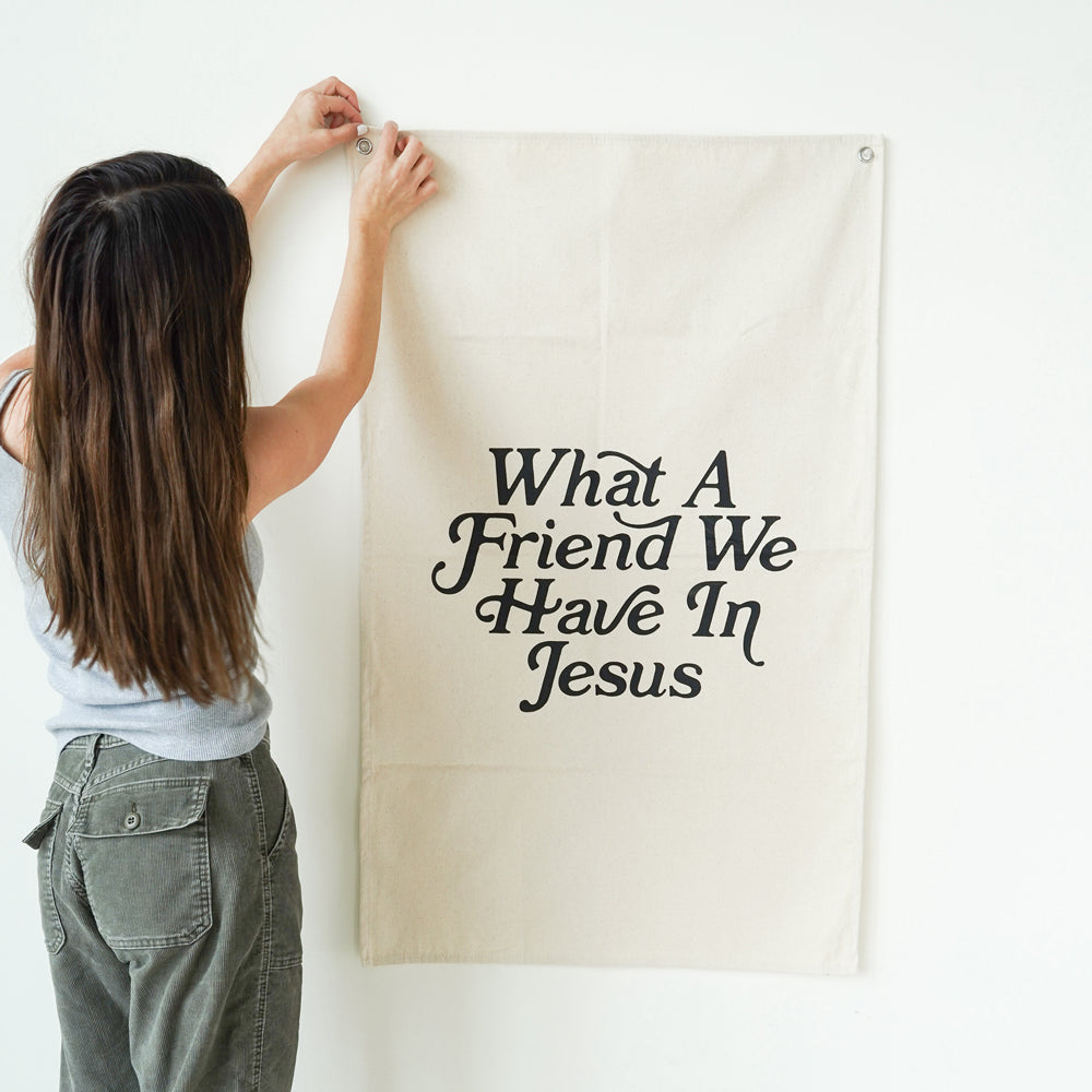 Person holding a banner with text 'What A Friend We Have In Jesus' against a white wall