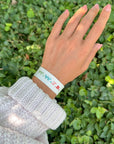 White WWJD bracelet with colorful lettering worn on a wrist beside green foliage
