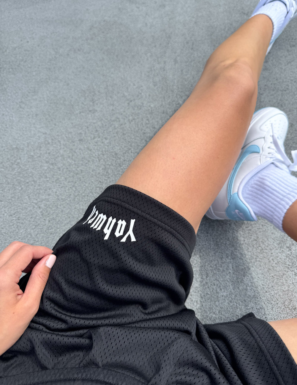 Overhead view of black Yahweh mesh shorts styled with white sneakers