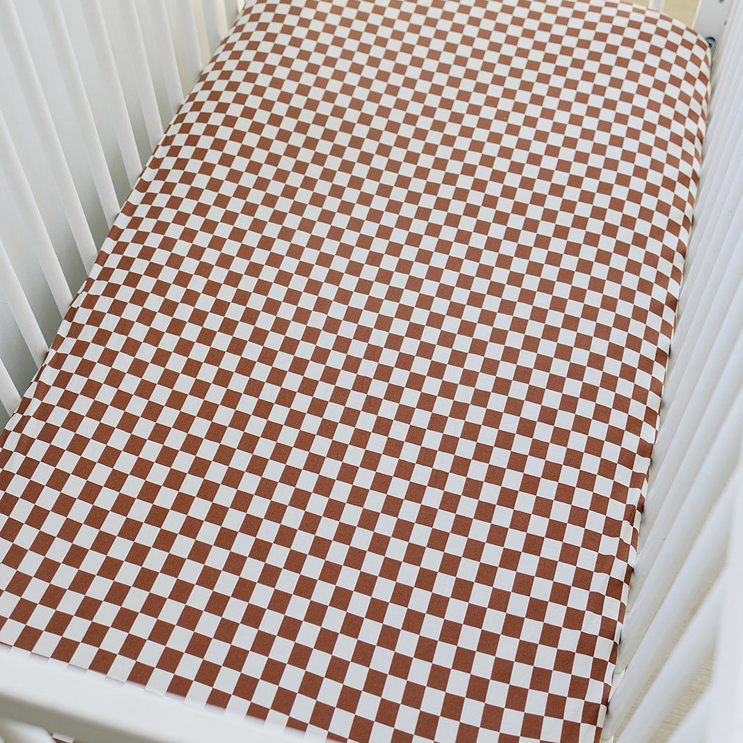 Checkered brown and white crib sheet on a white crib