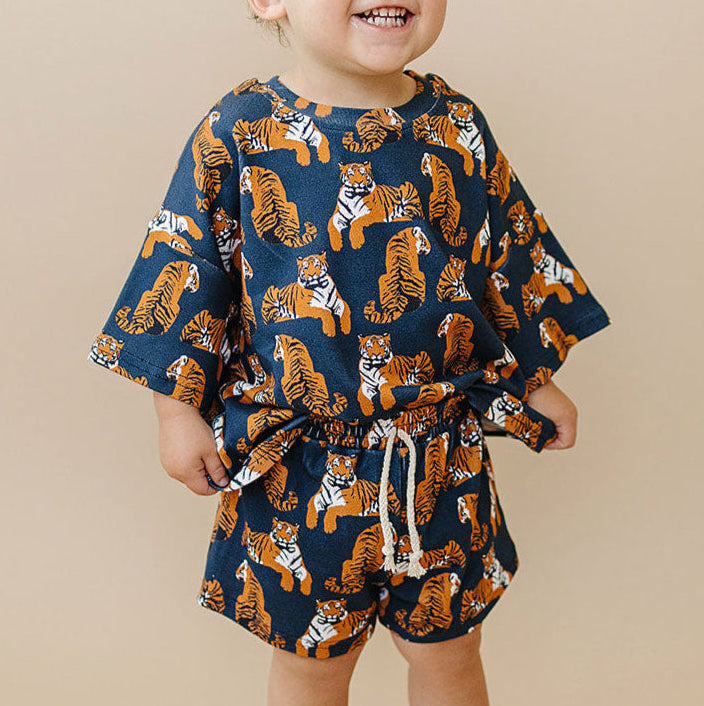 Child wearing a navy blue outfit with orange tiger pattern on a beige background