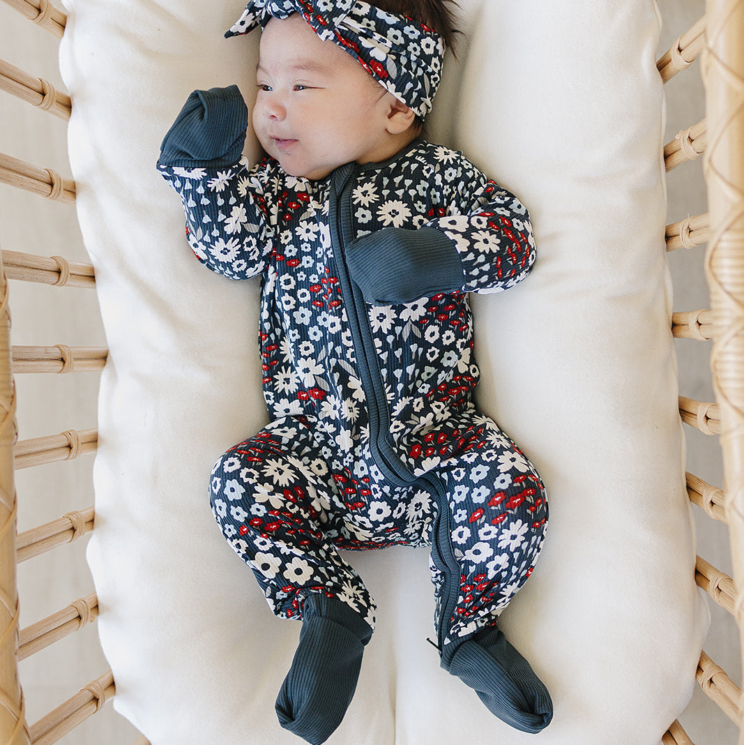 Baby in a floral outfit and headband lying in a crib with white mattress